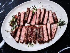 sliced steak on a white plate with rosemary garnish