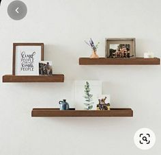 two wooden shelves with pictures and other items on them against a white wall in a living room