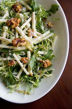 a white plate topped with lettuce and nuts on top of a wooden table