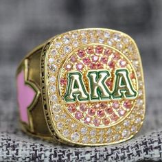 a ring with the letters aka in green and pink surrounded by small white diamonds