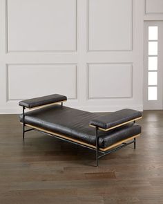 a black leather chaise lounge chair sitting on top of a hard wood floor next to a white wall