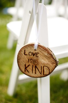 a wooden sign that says love is kind hanging from a white chair