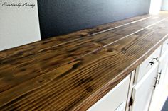 a wooden counter top in a kitchen with white cabinets and black painted wall behind it