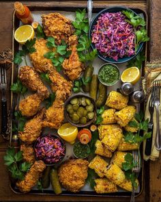 a platter filled with chicken, coleslaw and pickles next to other foods