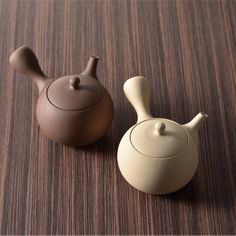 two ceramic teapots sitting on top of a wooden table next to each other