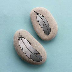 two rocks with feathers painted on them sitting next to each other in front of a blue background