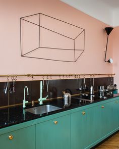 a kitchen with green cabinets and black counter tops in front of a pink painted wall