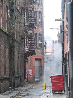 an alleyway with fire escapes and graffiti on the walls, next to a red dumpster