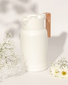 a white vase sitting next to flowers and a wooden handle on a white table top