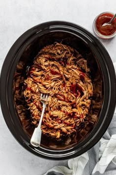 a slow cooker filled with pulled pork and bbq sauce next to a spoon