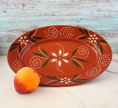 an orange sitting on top of a white counter next to a plate with flowers and leaves