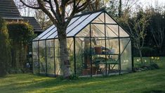 a small greenhouse in the middle of a yard with potted plants and trees around it