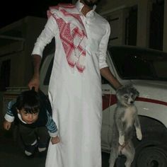 a man standing next to a little boy in front of a car with a dog