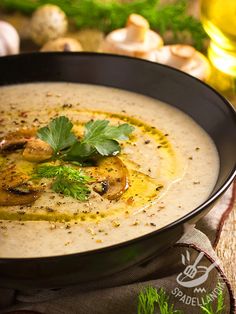 a black bowl filled with soup on top of a wooden table next to garlic and parsley