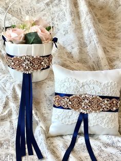 two white flower pots with blue ribbons and flowers in them on a bed next to a pillow