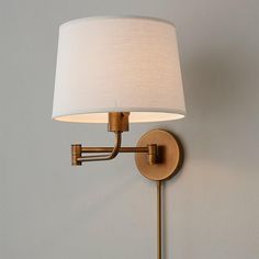 a wall light with a white shade on the side and a beige lamp hanging from it's arm