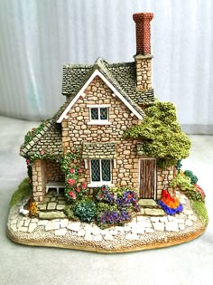 a figurine of a brick house with flowers and plants on the front lawn