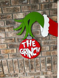 the grinch sign is hanging on a brick wall next to a red and white christmas ornament