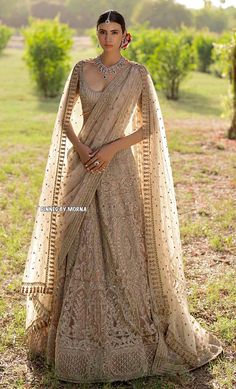 a woman in a beige lehenga standing on the grass with her arms around her neck