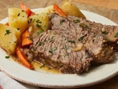 a white plate topped with meat, potatoes and carrots on top of a wooden table