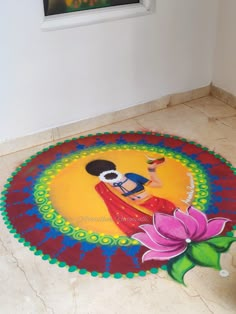 a colorful painting on the floor with a flower in front of it and a window behind it