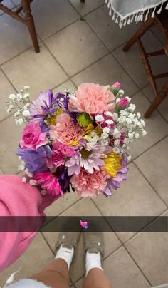 a person holding a bouquet of flowers in their hand while standing on tiled flooring