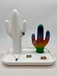 a white tray with a cactus, ring and other items on it that are sitting next to each other