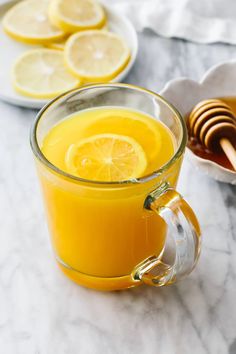 a glass mug filled with orange juice next to sliced lemons and honey on a marble table