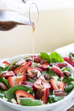 someone pouring dressing onto a salad with strawberries and spinach