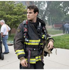 a firefighter is standing on the sidewalk with his gear in hand and looking at the camera