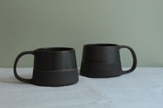 two black mugs sitting on top of a white sheet