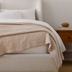 a bed with white linens and pillows in a small room next to a night stand