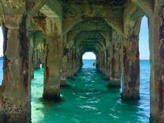 an old pier in the middle of the ocean with water underneath it and rocks on both sides