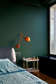 a bedroom with green walls and a bed in the foreground, an orange lamp on the wall