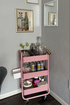 a pink cart with drinks on it sitting in front of a mirror and framed pictures