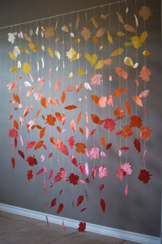 a mobile made out of paper leaves hanging from the side of a wall in front of a gray wall