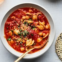 a white bowl filled with pasta and sauce on top of a table next to bread