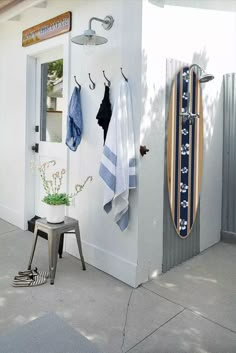 a white building with two surfboards hanging on it's wall and a stool outside