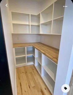 an empty walk in closet with white shelving and wood flooring on the side