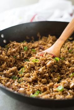 a skillet filled with rice and meat on top of a table next to a wooden spoon