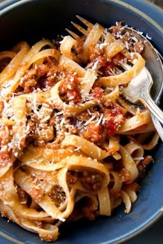 a blue bowl filled with pasta covered in sauce and parmesan cheese on top