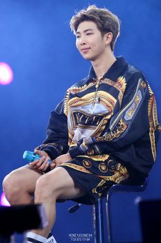 a man sitting on top of a chair wearing a black shirt and shorts with gold designs