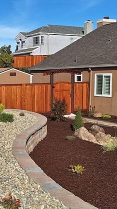 a house with a wooden fence next to it and landscaping in front of the house