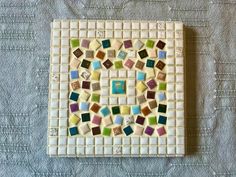 a white tile with multicolored glass tiles on the top and bottom, sitting on a bed