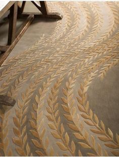 an area rug with gold leaf designs on the floor and in front of a wooden table