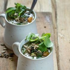 two white mugs filled with soup on top of a wooden table