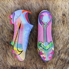 two colorful soccer cleats laying on top of a fur covered ground with one shoe in the middle