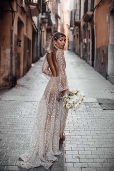 a woman in a long dress standing on a brick street holding a white bouquet and looking off into the distance