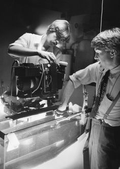 black and white photograph of two men working on a projector in a room with other people