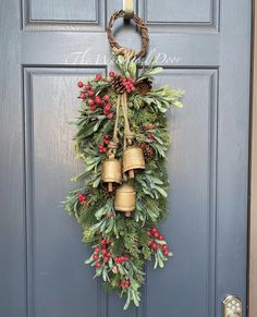 a christmas wreath hanging on the front door with bells and evergreen leaves, berries and pine cones